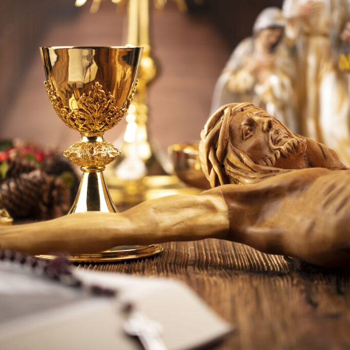 The Cross, monstrance, Jesus figure, Holy Bible and golden chalice on the rustic wooden table.